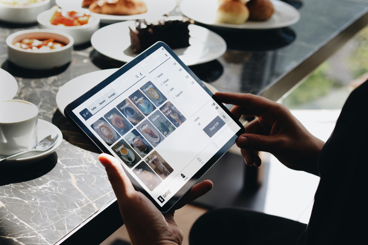 Une personne consulte la carte d'un restaurant sur une tablette, à côté d'une table servie